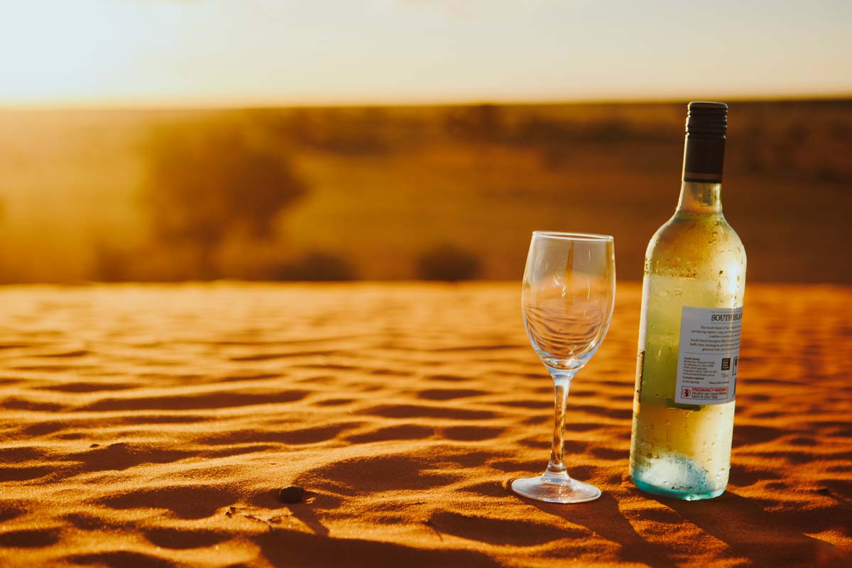 Bottle of wine and glass on sandhill at sunset