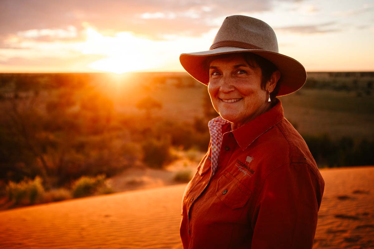 Woman in outback hat smiling at the camera with sunset in the distance