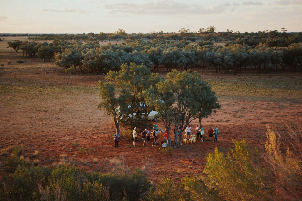 Group of people under trees in vast outback setting